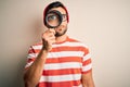 Young detective man looking through magnifying glass over isolated background with a confident expression on smart face thinking