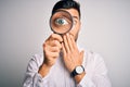 Young detective man looking through magnifying glass over isolated background cover mouth with hand shocked with shame for Royalty Free Stock Photo