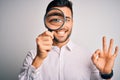 Young detective man looking through magnifying glass over isolated background doing ok sign with fingers, excellent symbol Royalty Free Stock Photo