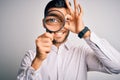 Young detective man looking through magnifying glass over isolated background with happy face smiling doing ok sign with hand on Royalty Free Stock Photo