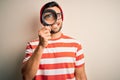 Young detective man looking through magnifying glass over isolated background with a happy face standing and smiling with a Royalty Free Stock Photo