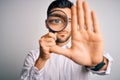 Young detective man looking through magnifying glass over isolated background with open hand doing stop sign with serious and Royalty Free Stock Photo