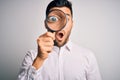 Young detective man looking through magnifying glass over isolated background scared in shock with a surprise face, afraid and Royalty Free Stock Photo