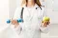 Young dietitian with apple and dumbbell at clinic