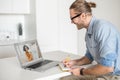 Young diligent employee sitting at the table and writing down while looking at the laptop