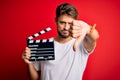 Young director man with beard making movie using clapboard over isolated red background with angry face, negative sign showing