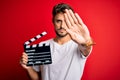 Young director man with beard making movie using clapboard over isolated red background with open hand doing stop sign with Royalty Free Stock Photo