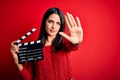 Young director woman with blue eyes making movie holding clapboard over red background with open hand doing stop sign with serious Royalty Free Stock Photo