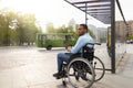 Young disabled black man in wheelchair waiting for public transport on bus stop, having difficulty traveling around city Royalty Free Stock Photo