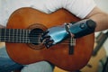 Young disabled man with artificial prosthetic hand plays on guitar at shop.