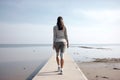 A young disabled woman with prosthetic legs in a gray tracksuit poses against the backdrop of the sea in sunny weather