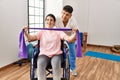 Young disabled woman sitting on wheelchair making mobility exercise using elastic band at the clinic