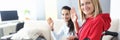 Young disabled woman in wheelchair with helper is sitting by laptop screen and waving hello