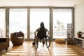 Young disabled woman in wheelchair at home, rear view.