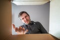 Young disappointed and displeased man is opening gift and looking inside cardboard box. Royalty Free Stock Photo