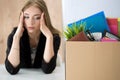 Young dismissed female worker sitting near the carton box with h