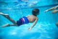 Young diverse boy swimming underwater in a swimming pool. Learning to swim with the help of his parent. Royalty Free Stock Photo