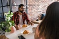 Young diverse loving couple eating croissant and talks together at home in breakfast time. Communication and