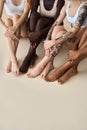 Young diverse women wearing underwear sitting on beige showing smooth legs.