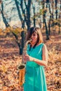 Young divine dark-haired woman in a long blue dress plays the alto saxophone against the background of foliage fallen from the tre Royalty Free Stock Photo