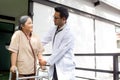 Young doctor assistance elderly patient while guidance therapy with walker in garden at hospital.