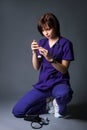 A young doctor in a blue coat on a gray background holds in his hand a syringe with medicine. Medical worker