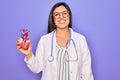 Young doctor cardiology specialist woman holding medical heart over pruple background with a happy face standing and smiling with