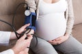 Young doctor is checking blood pressure of pregnant woman at home. High pressure problem during pregnancy concept Royalty Free Stock Photo