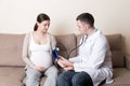 Young doctor is checking blood pressure of pregnant woman at home. High pressure problem during pregnancy concept Royalty Free Stock Photo