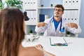 Young doctor with client at medical clinic looking confident with smile on face, pointing oneself with fingers proud and happy Royalty Free Stock Photo