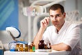 Young doctor dentist man in uniform sitting near dental chair in dental office in clinic with equipment at background Royalty Free Stock Photo