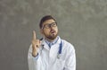 Young doctor in glasses and lab coat with stethoscope thinking with one finger pointing up Royalty Free Stock Photo