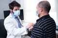 Young doctor listening to mature man patient heart and lungs with a stethoscope Royalty Free Stock Photo