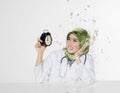 Young doctor with hijab with happy face expression siiting in front desk holding alarm clock Royalty Free Stock Photo