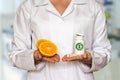 Young doctor holding two halves of orange and bottle of pills wi