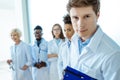 Young doctor in lab coat holding clipboard with group of young doctors in lab coats standing Royalty Free Stock Photo