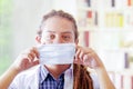 Young doctor with long dread locks posing for camera, adjusting facial mask covering mouth, clinic in background