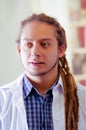 Young doctor with long dread locks posing for camera, clinic in background, medical concept