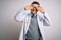 Young doctor man with blue eyes wearing medical coat and stethoscope over isolated background covering eyes with hands smiling Royalty Free Stock Photo