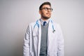 Young doctor man with blue eyes wearing medical coat and stethoscope over isolated background looking away to side with smile on Royalty Free Stock Photo