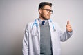 Young doctor man with blue eyes wearing medical coat and stethoscope over isolated background Looking proud, smiling doing thumbs Royalty Free Stock Photo
