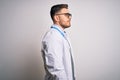 Young doctor man with blue eyes wearing medical coat and stethoscope over isolated background looking to side, relax profile pose Royalty Free Stock Photo