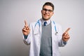 Young doctor man with blue eyes wearing medical coat and stethoscope over isolated background smiling confident pointing with Royalty Free Stock Photo