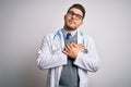 Young doctor man with blue eyes wearing medical coat and stethoscope over isolated background smiling with hands on chest with Royalty Free Stock Photo