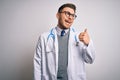 Young doctor man with blue eyes wearing medical coat and stethoscope over isolated background smiling with happy face looking and Royalty Free Stock Photo