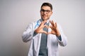 Young doctor man with blue eyes wearing medical coat and stethoscope over isolated background smiling in love doing heart symbol Royalty Free Stock Photo