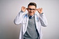 Young doctor man with blue eyes wearing medical coat and stethoscope over isolated background Smiling pulling ears with fingers,