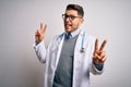 Young doctor man with blue eyes wearing medical coat and stethoscope over isolated background smiling with tongue out showing Royalty Free Stock Photo