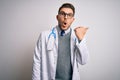 Young doctor man with blue eyes wearing medical coat and stethoscope over isolated background Surprised pointing with hand finger Royalty Free Stock Photo