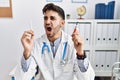 Young doctor man holding electronic cigarette at medical clinic angry and mad screaming frustrated and furious, shouting with Royalty Free Stock Photo